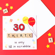30 is only 12 in Scrabble. 30th Birthday Card. Illustrated with party balloons and confetti and hand finished with wooden scrabble tiles. on a red background. 