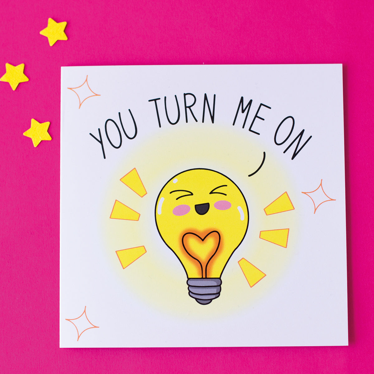 Funny valentine's anniversary card. Cute illustration of a lightbulb saying you turn me on. sat on a pink background with yellow stars