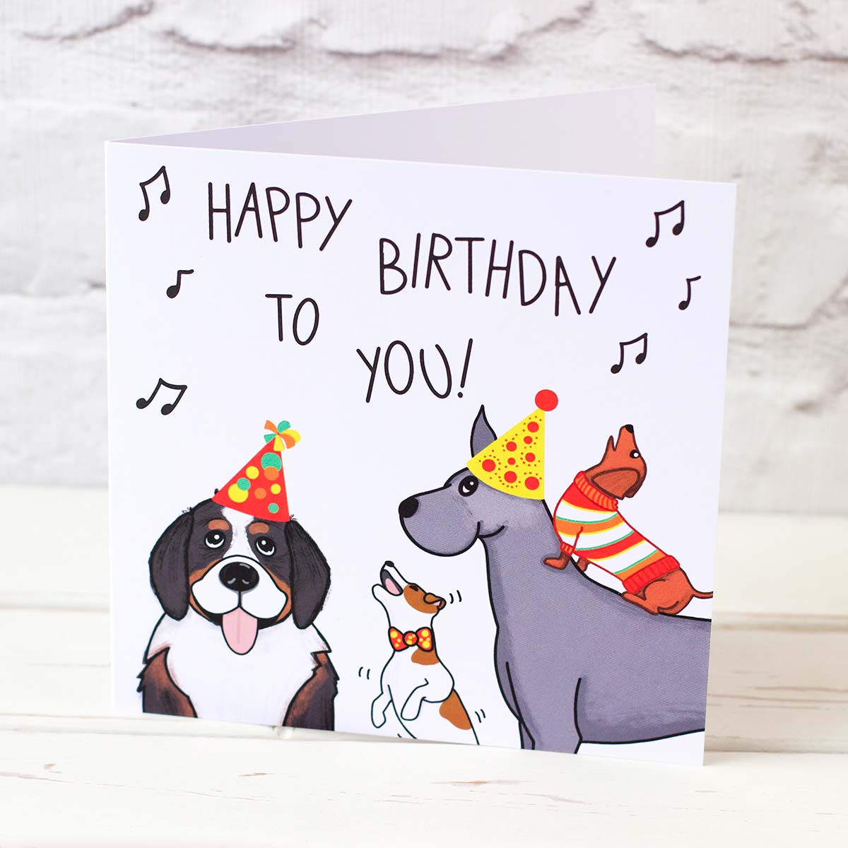 Large and small breeds in party outfits singing Happy Birthday in a card that is stood up