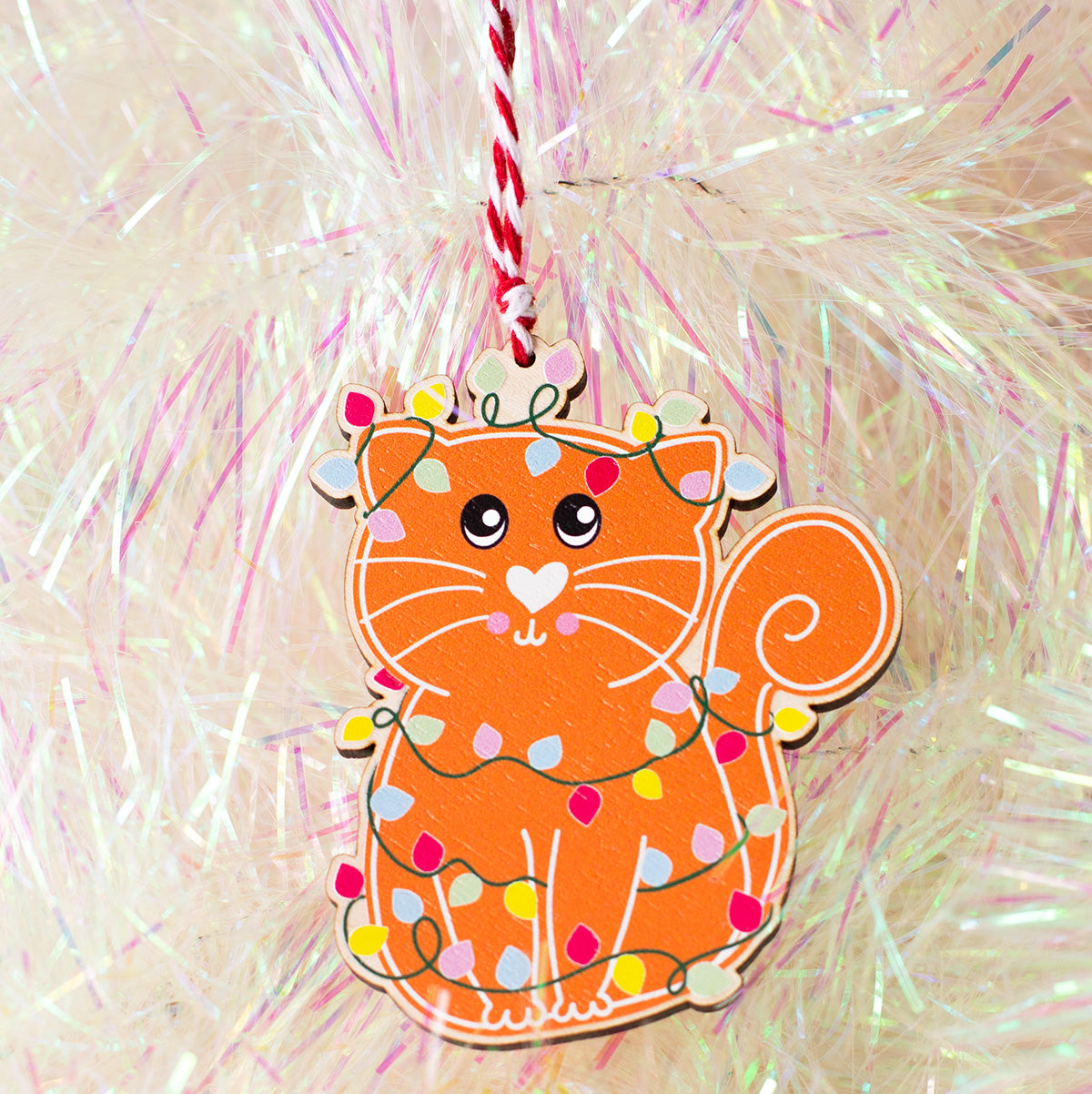 Christmas tree wooden ornament of a cat illustrated in a gingerbread style with fairy lights