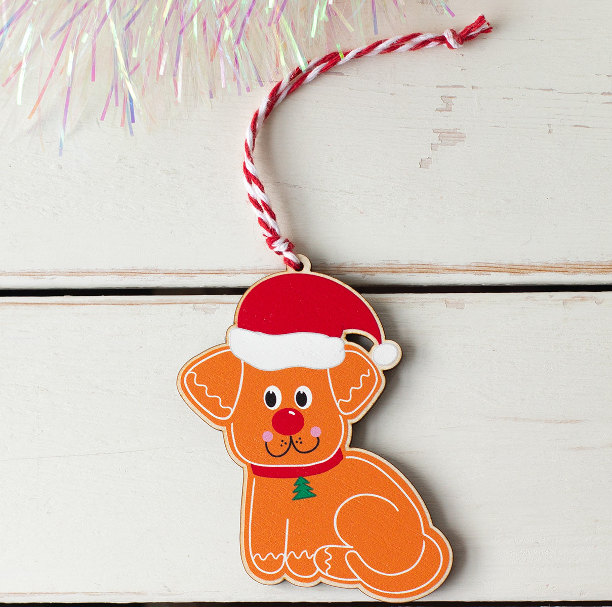 Wooden tree decoration of a dog with a red nose and santa hat illustrated in a gingerbread style, printed on to maple veneered MDF.